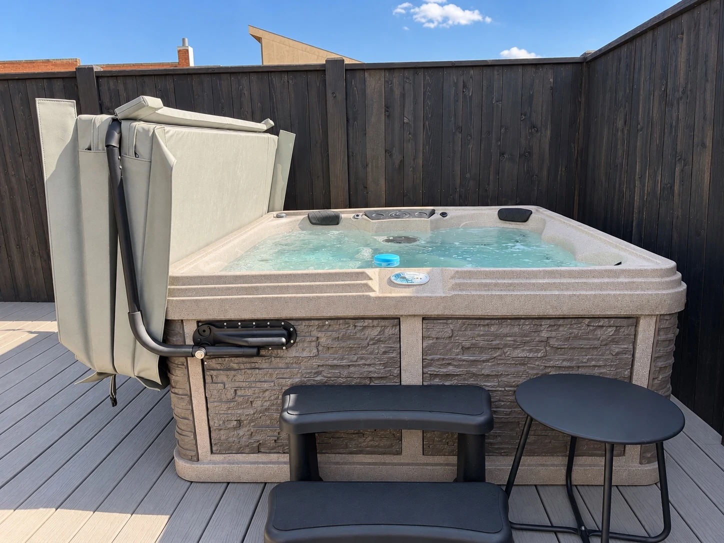 Hot tub with open cover on a deck beside a privacy fence