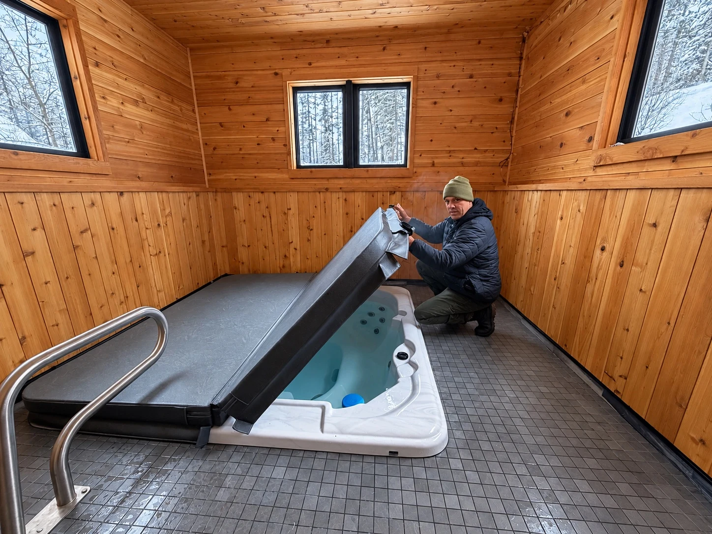 Technician lifting the cover of an indoor hot tub in a wood-paneled room