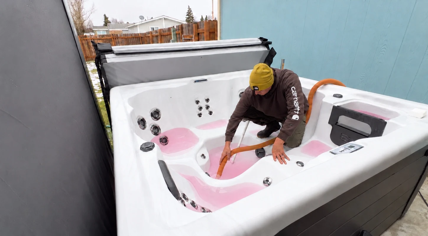 Technician vacuuming pink antifreeze from the low spots of a drained hot tub