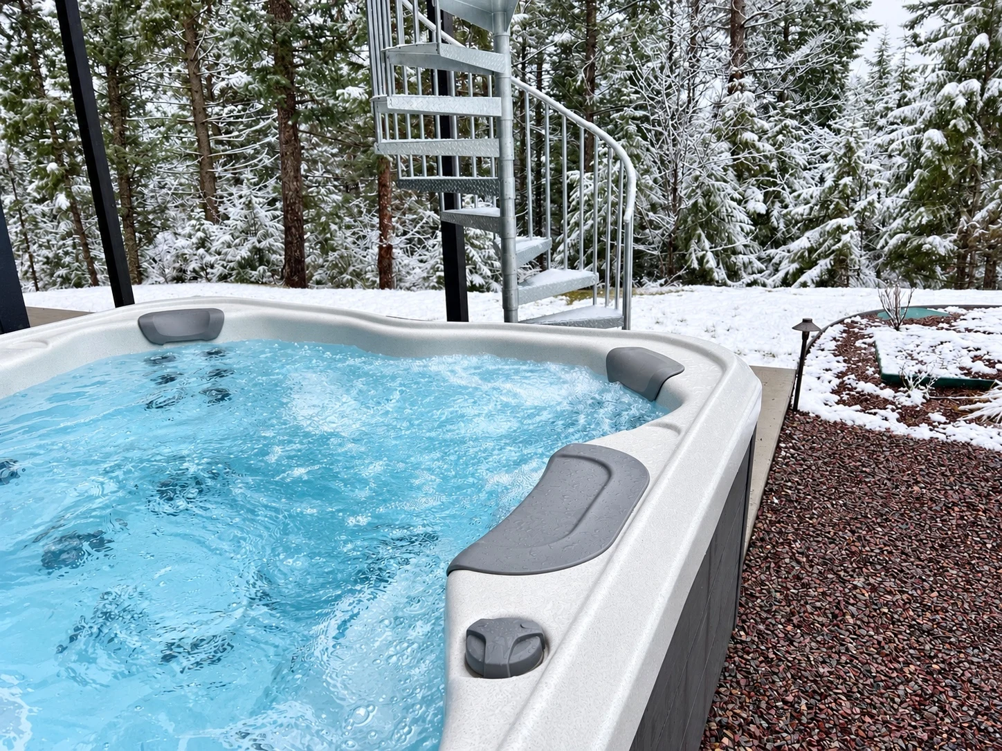 Outdoor hot tub with bubbling blue water beside snow-covered evergreen trees